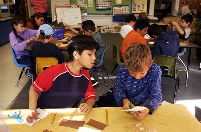 Two students sitting at a desk cutting paper