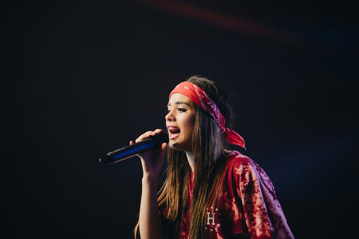 A young woman wearing a red bandana and read outfit sings into a mic