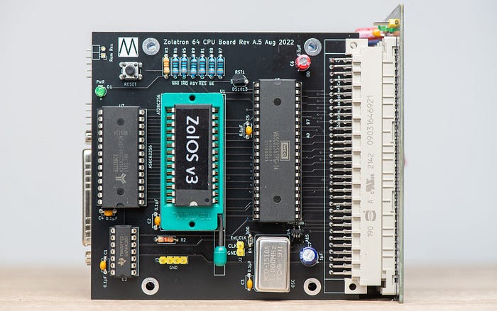 Photograph of an electronics circuit board. There are three large chips, the centre one of which has a label ‘ZolOS v3’ and is held in a large, turquoise socket.