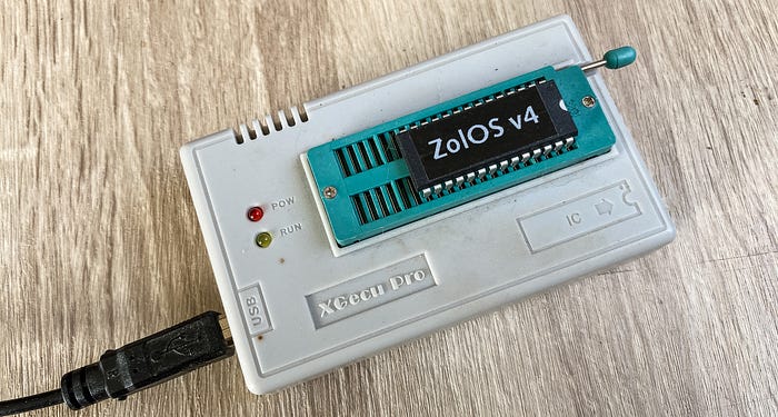 Photograph of an electronic device — basically a small beige box with a turquoise-coloured chip socket on the top. A chip with the label ‘ZolOS v4’ is plugged into the socket.