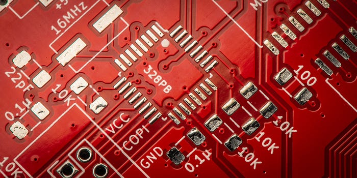 Close-up photograph of the unpopulated surface of a printed circuit board, illustrating the sharpness of the silkscreening and how the solder mask runs between the pads for the ICs.