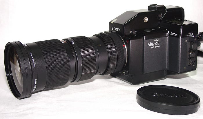 Product photo of a reflex camera with a long lens. A removed lens cap is in the foreground.