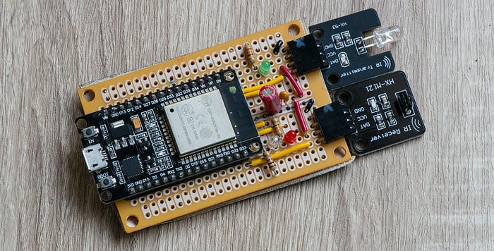Close-up photograph of an electronics circuit laid out on a prototyping board into which are soldered a microcontroller development board and two modules (right) carrying an infrared sensor and LED.