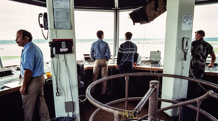 Photograph of the inside of an air traffic control tower at an airport with four people standing, looking out of the windows.