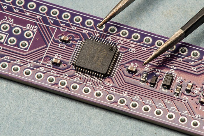 Close-up photograph of a electronic printer circuit board. In the top right are the prongs of a pair of tweezers demonstrating how small the components are.