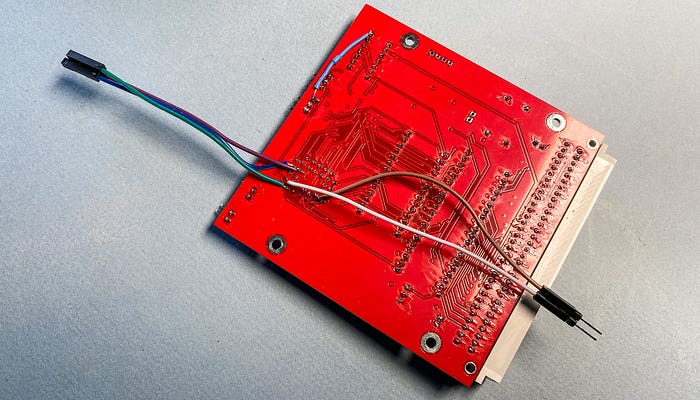 Close up photograph of a red printed circuit board with soldered-on wires.